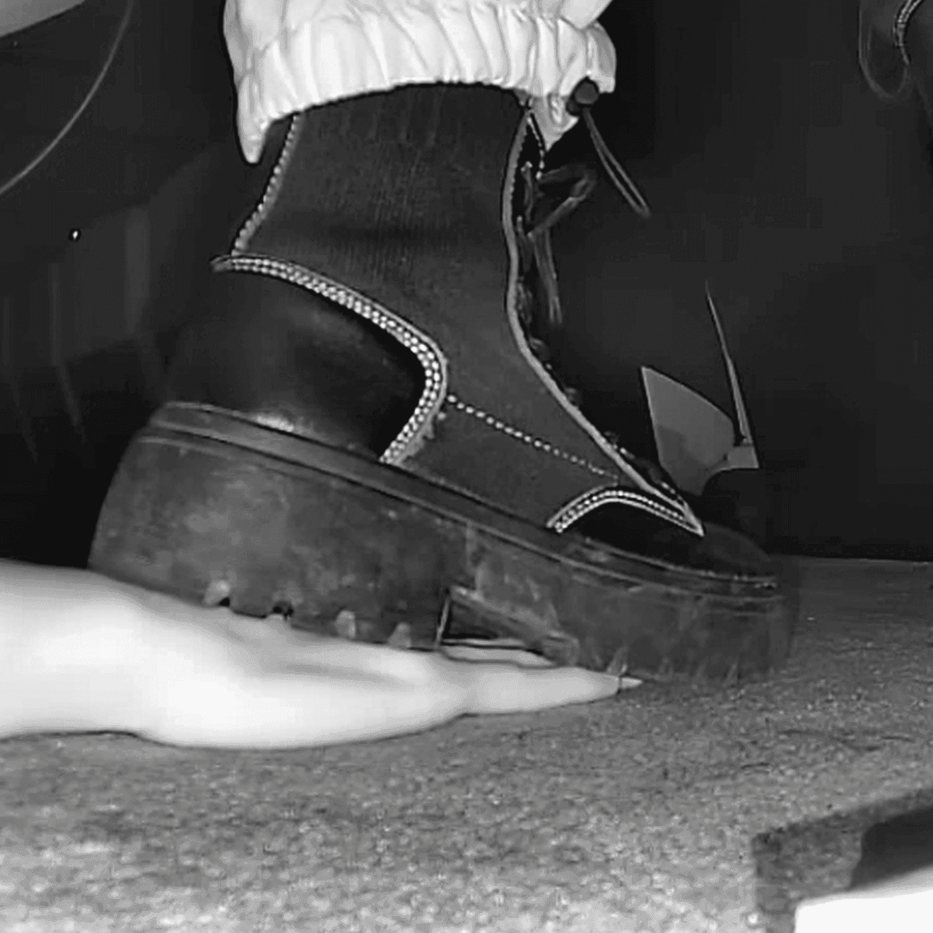 Woman unaware steps on hand with chunky-heeled black ankle boots in cinema
